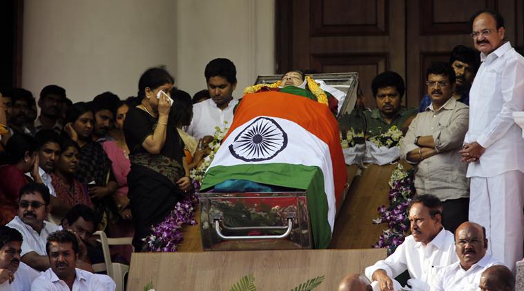 Sasikala Natarajan, left standing, a close friend of India's Tamil Nadu state former Chief Minister Jayaram Jayalalithaa, wipes her tears next to Jayalalithaa's body wrapped in the national flag and kept for public viewing outside an auditorium in Chennai, India, Tuesday, Dec. 6, 2016. Jayalalithaa, the hugely popular south Indian actress who later turned to politics and became the highest elected official in the state of Tamil Nadu, died Monday. She was 68. (AP Photo/Aijaz Rahi)